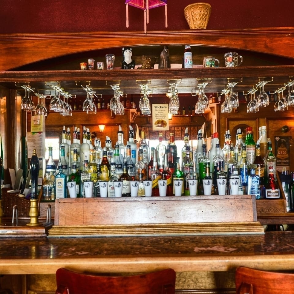 A fully stocked wooden bar with liquor bottles, beer taps, wine glasses, and bar stools.