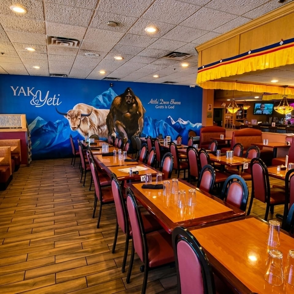 Spacious dining room at Yak & Yeti restaurant with booths, tables, and a large mural of a yak and yeti.