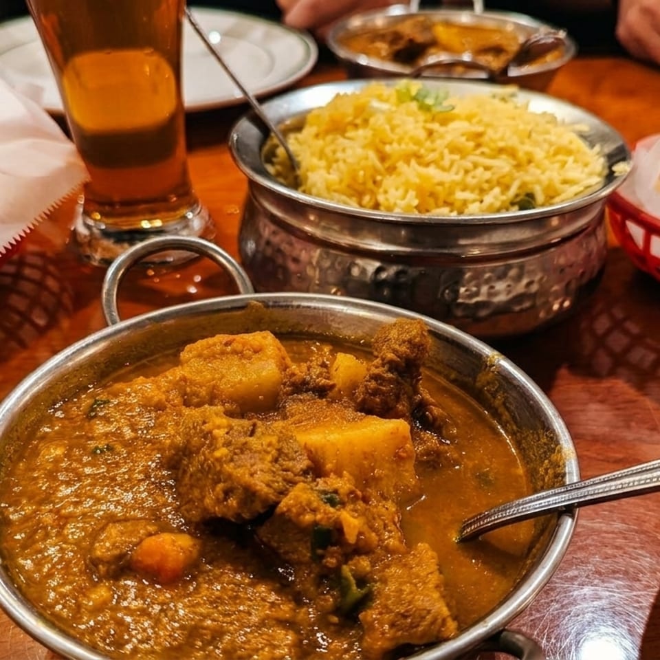 Indian dishes on a wooden table, including curry, rice, samosas, and naan.